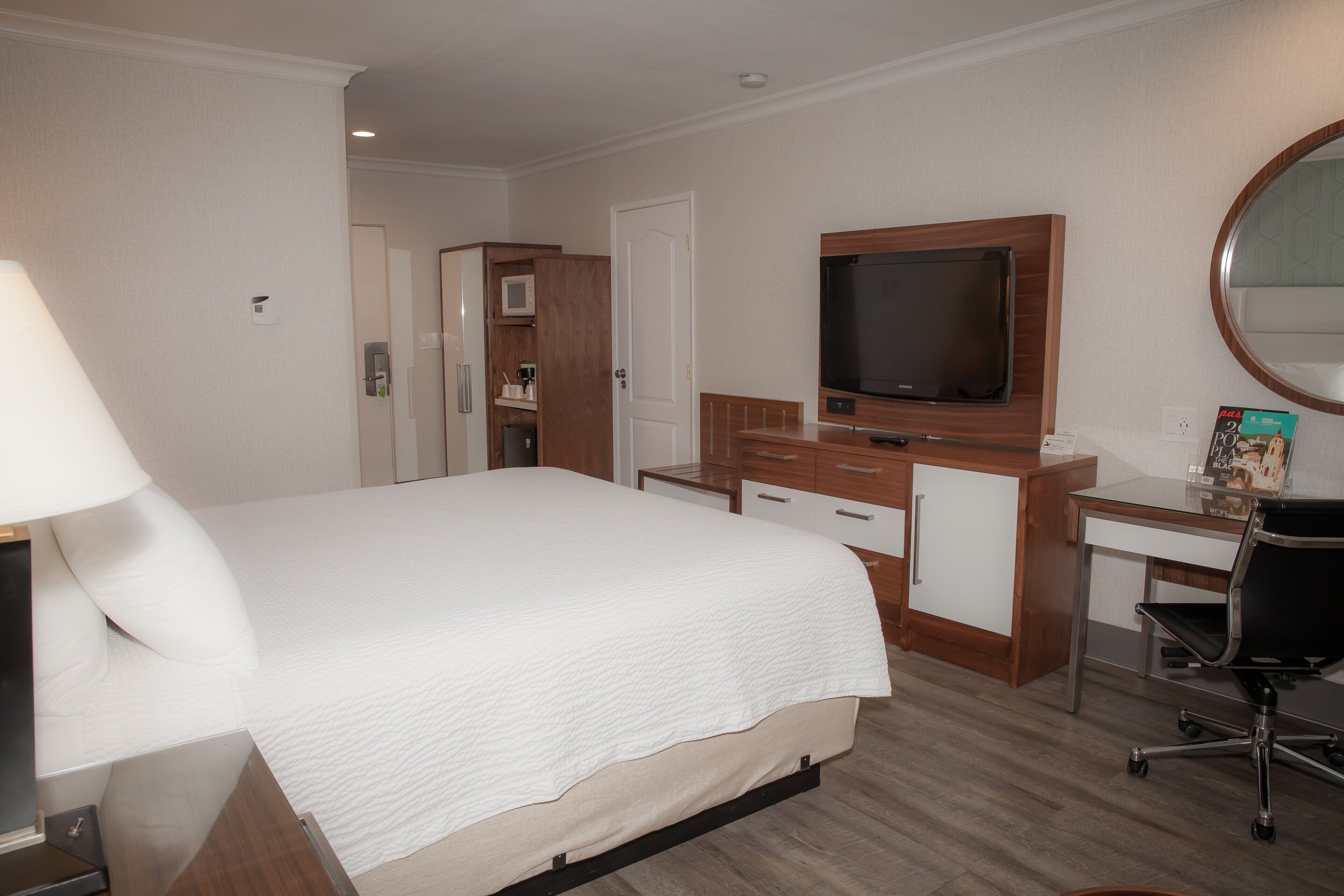 A hotel room with a bed, a desk with a chair, a television, a microwave, and a bathroom.