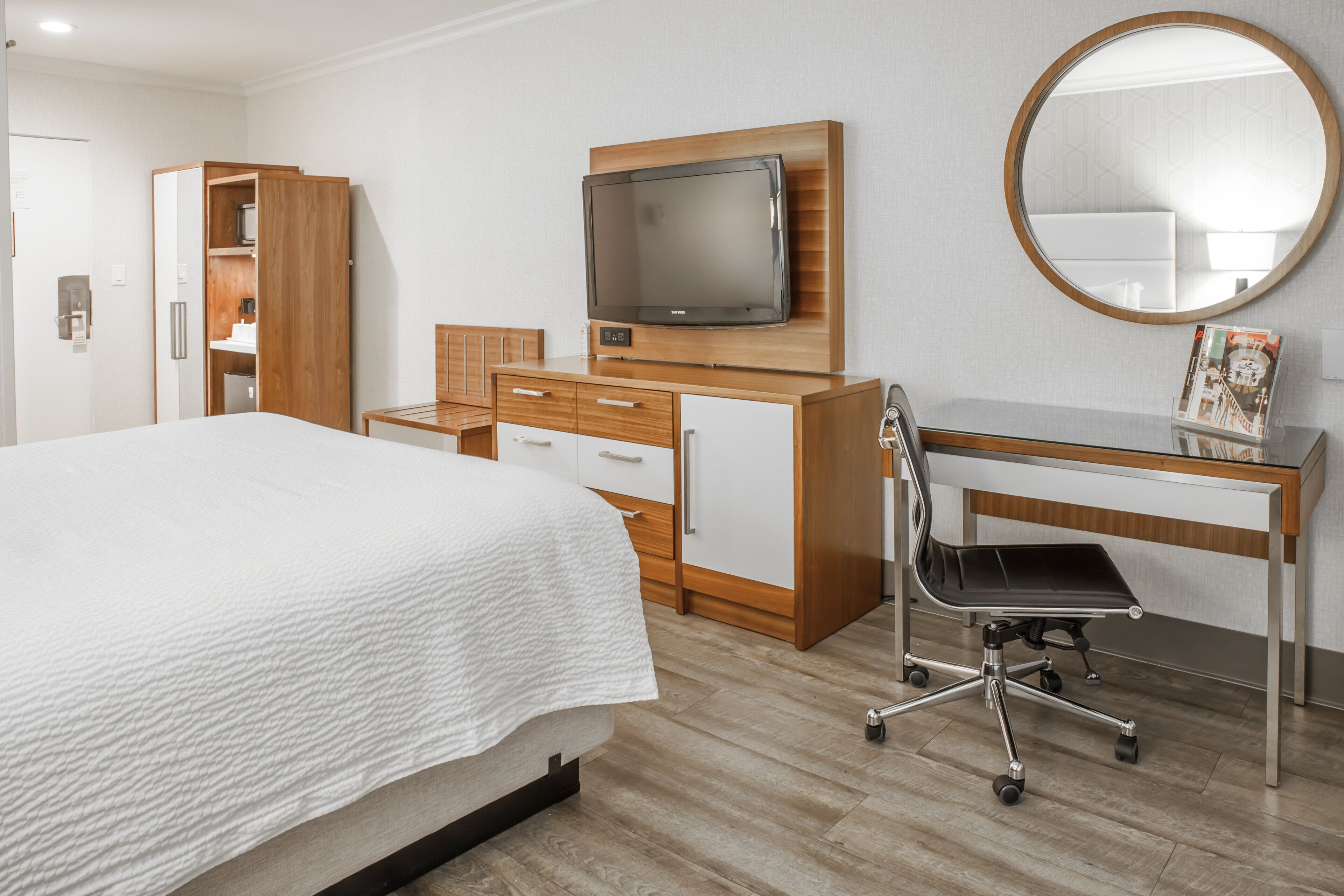 A hotel room with a bed, a desk with a chair, a television, and a wardrobe.