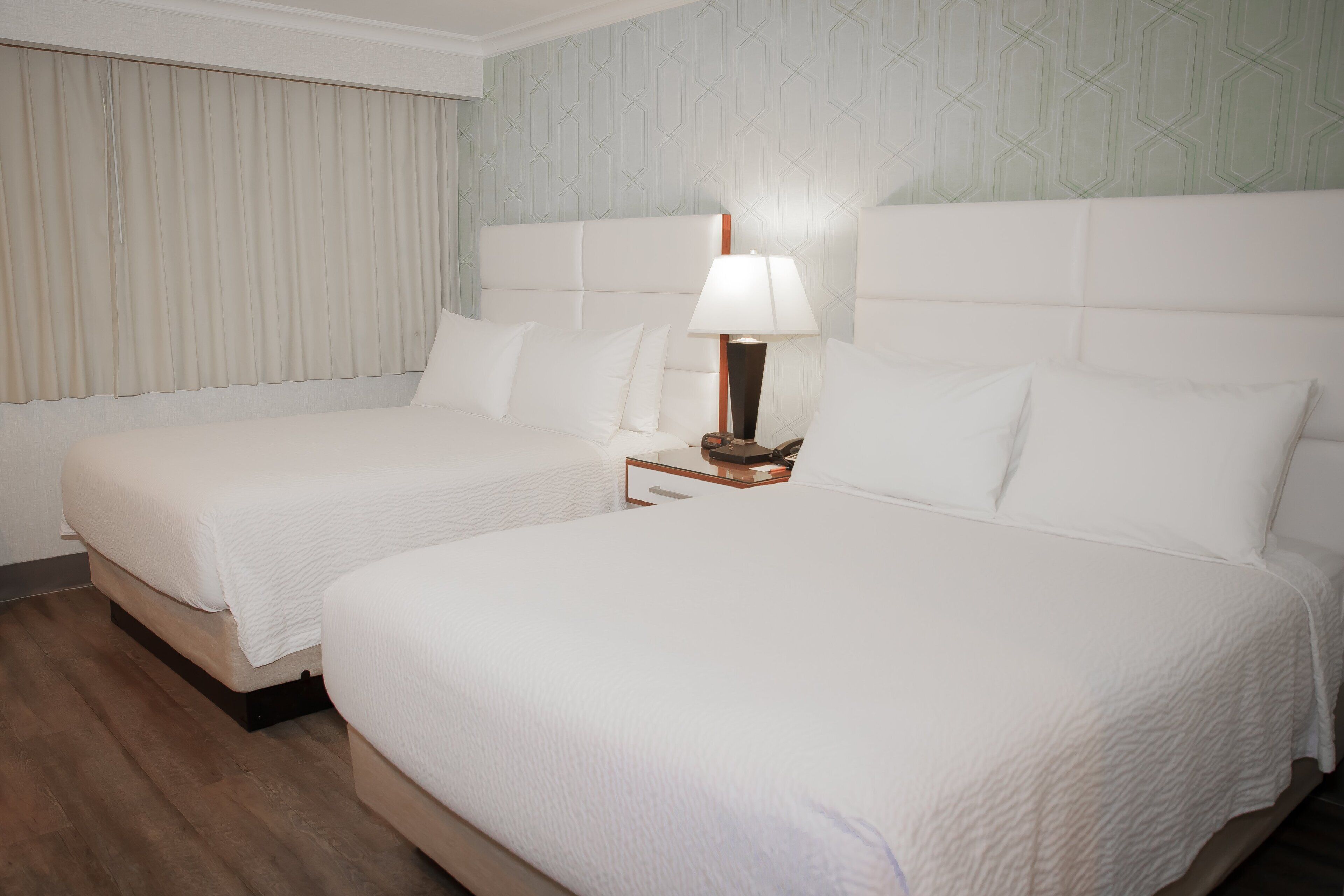 Een hotelkamer met twee bedden, een nachtkastje met een lamp en behang met een patroon.