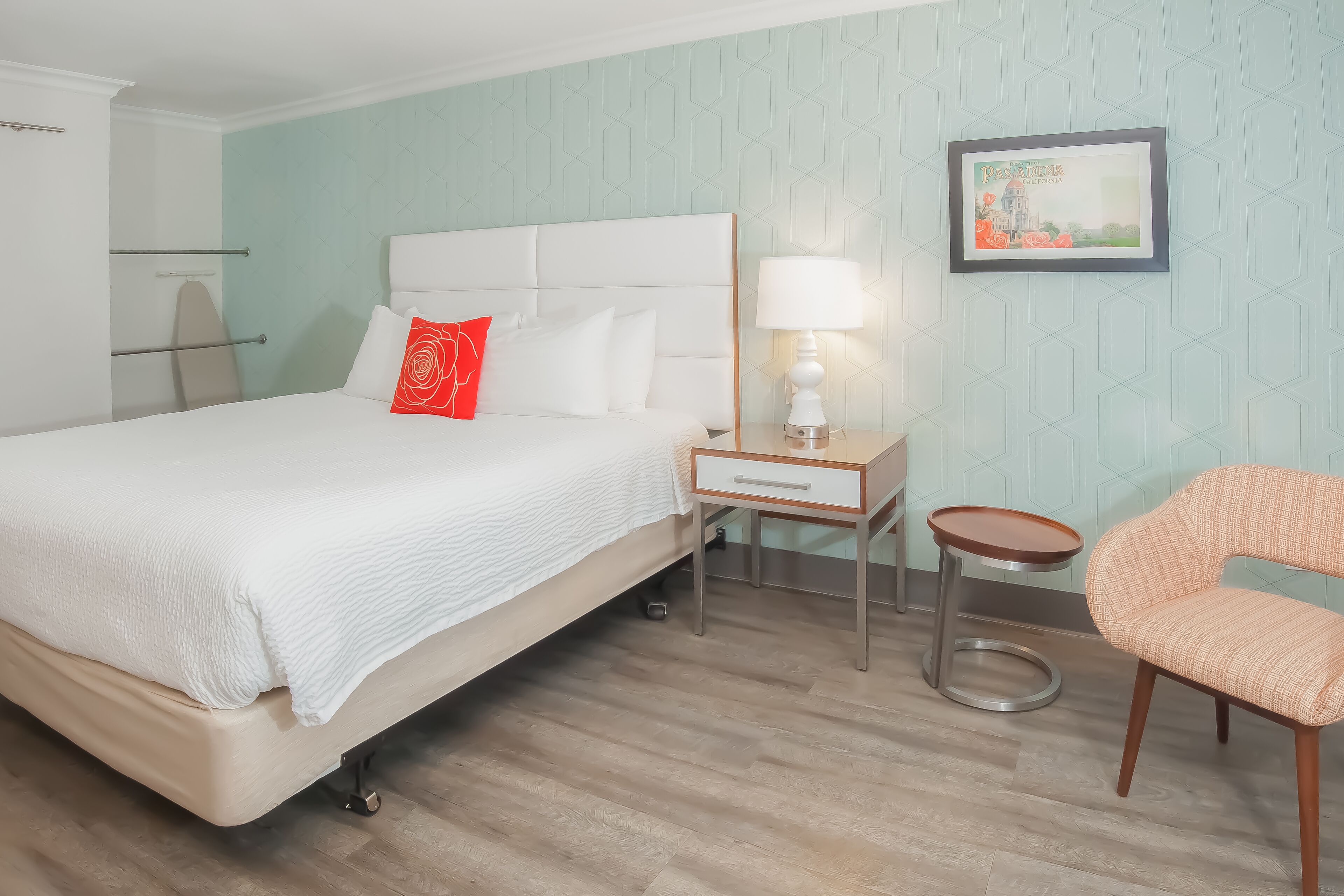 A hotel room with a bed, a nightstand with a lamp, a chair, and a framed picture on the wall.