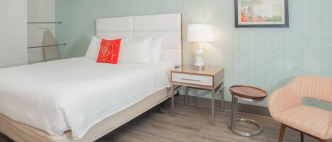 A hotel room with a bed, a nightstand with a lamp, a chair, and a framed picture on the wall.