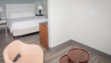 Una habitación de hotel con una cama, una mesita de noche con lámpara, una mesita auxiliar de madera y una silla.