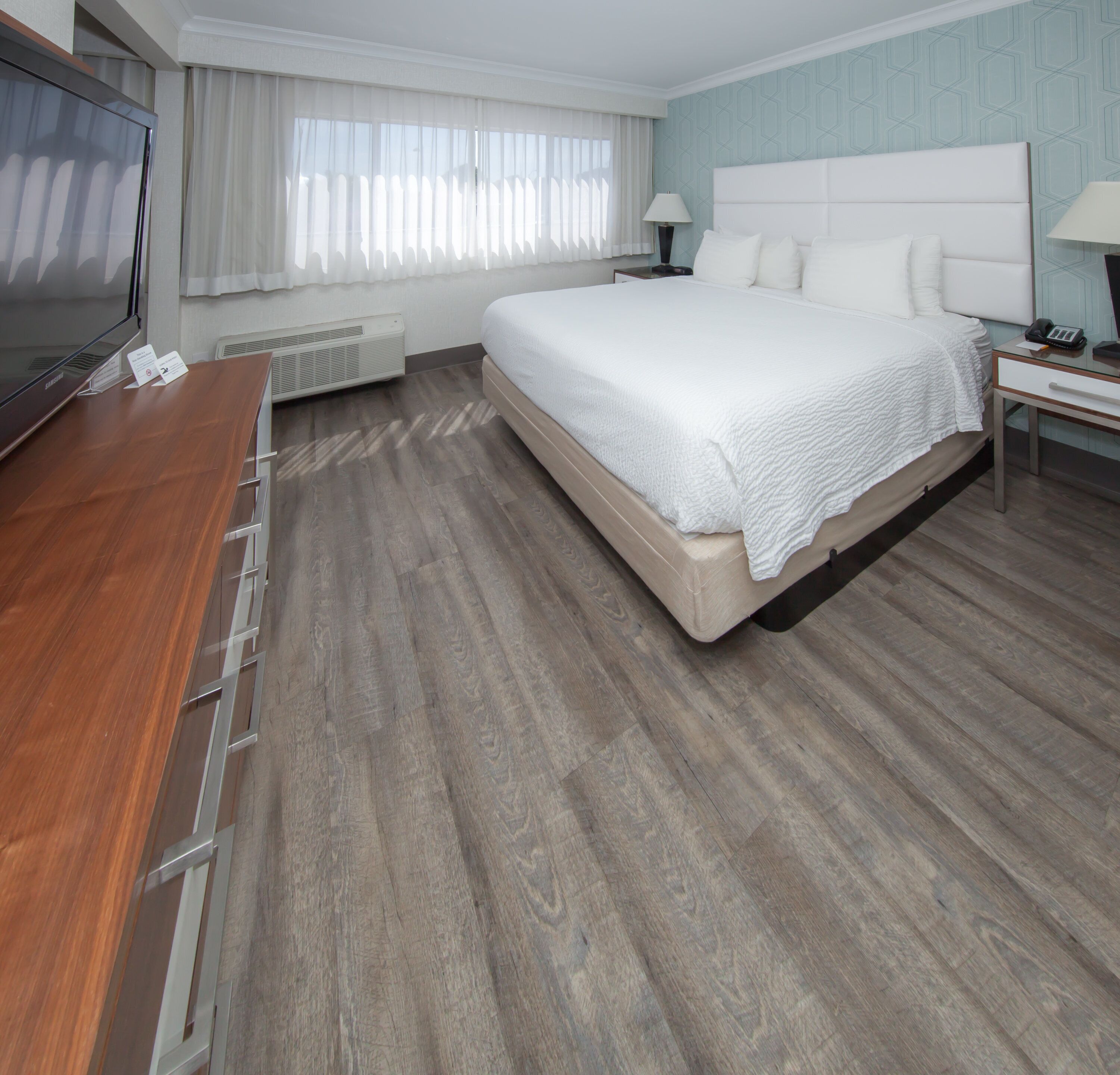 Una habitación de hotel con una cama grande, un escritorio de madera, un televisor y una ventana con cortinas.