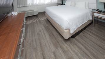 Una habitación de hotel con una cama grande, un escritorio de madera, un televisor y una ventana con cortinas.