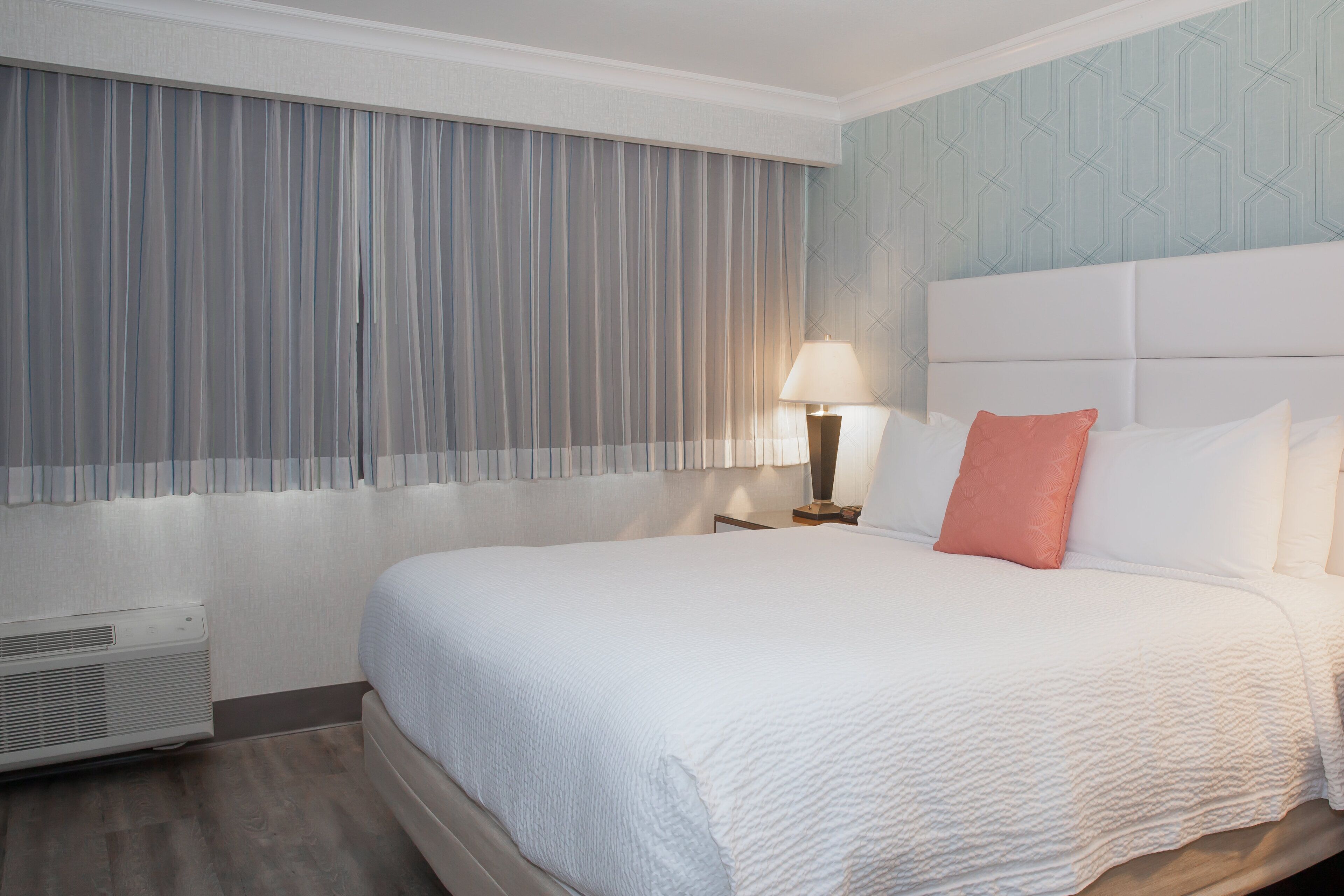 Een hotelkamer met een groot bed, een nachtkastje met een lamp en een muur met een geometrisch patroon.