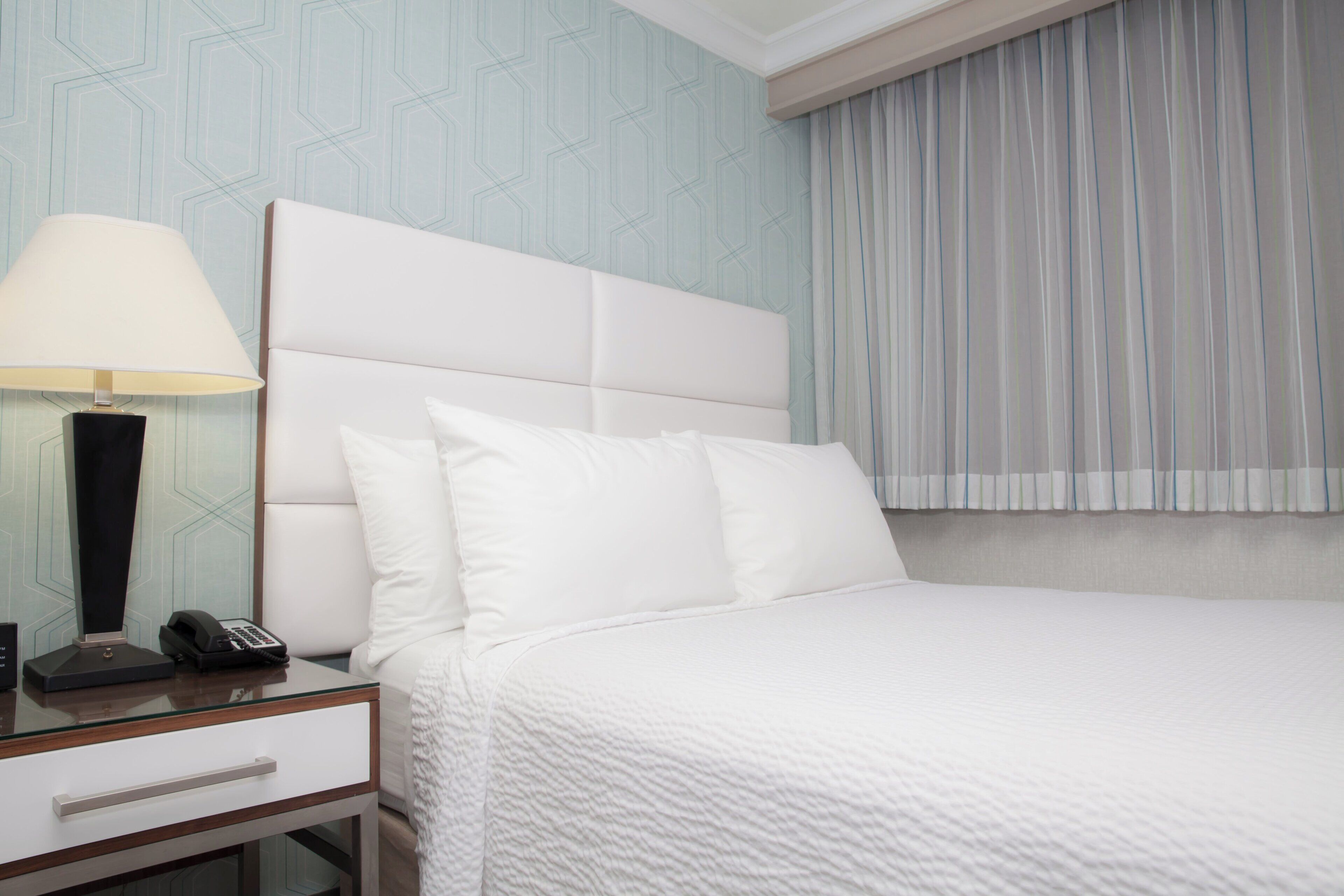 Une chambre d’hôtel avec un lit, une table de chevet avec une lampe et un téléphone.