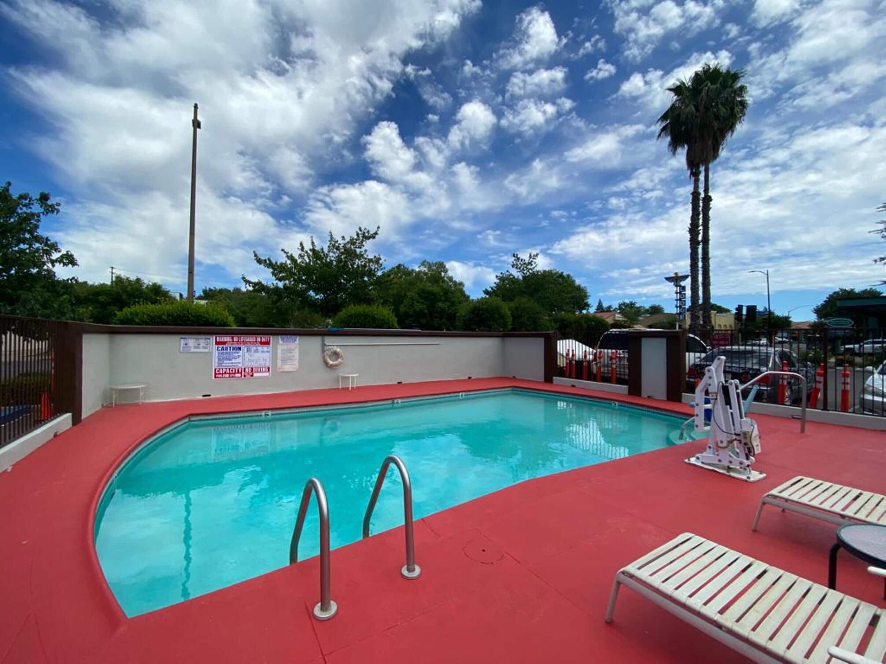 Une piscine dotée d’une plage rouge, de rampes métalliques et de chaises longues.