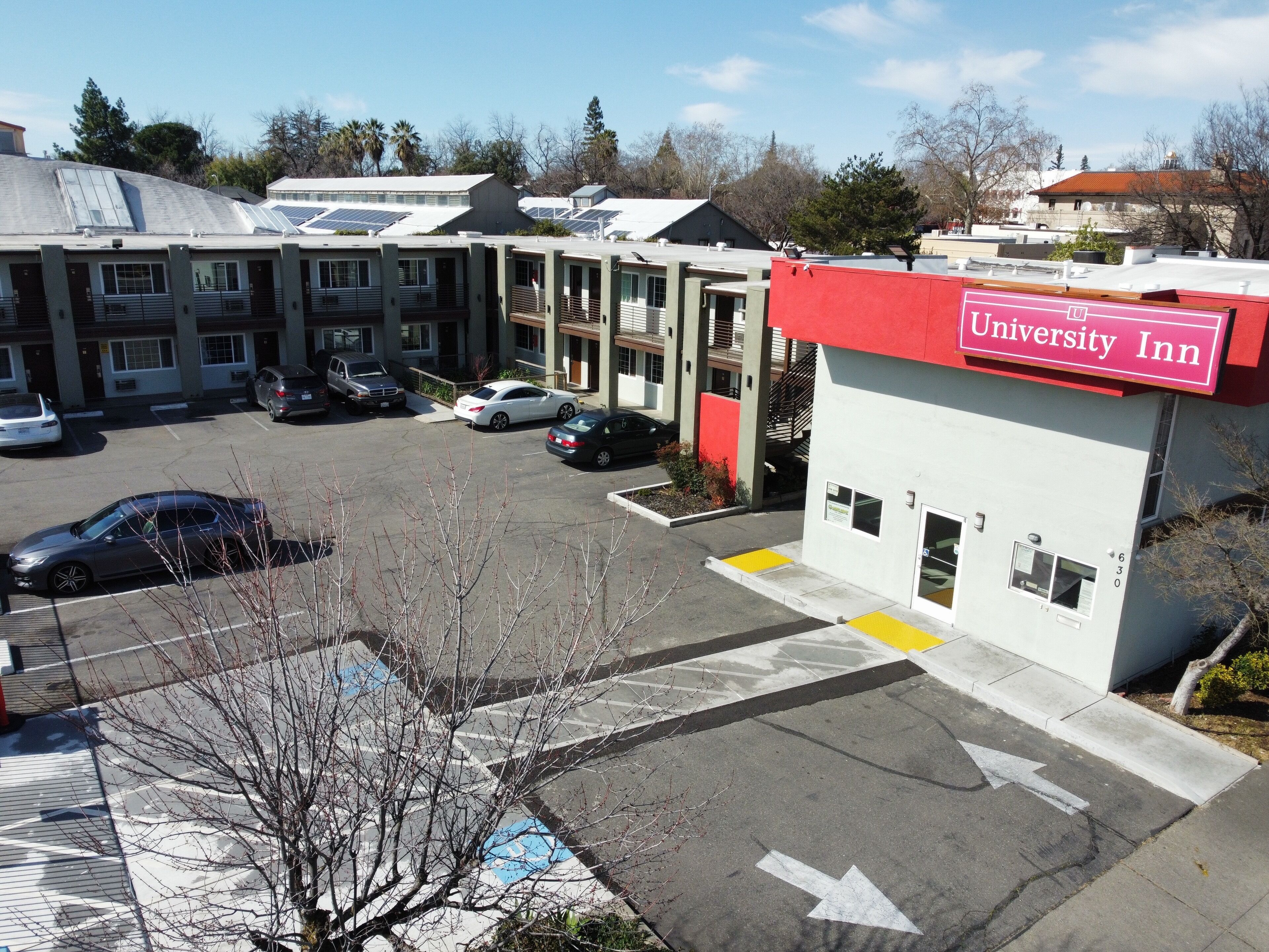 Edificio del University Inn con un toldo rojo, aparcamiento y varios coches estacionados frente a él.