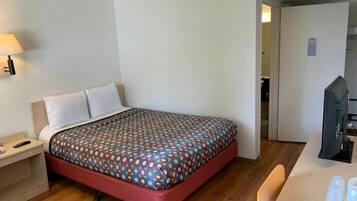 A hotel room with a single bed, a bedside table with a lamp, a desk with a computer, and a chair.