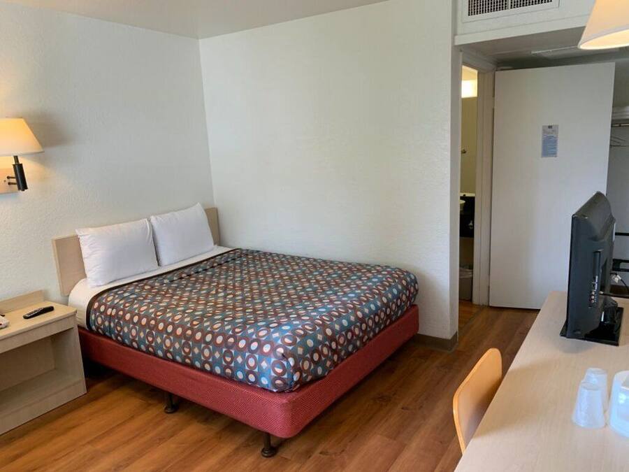 A hotel room with a single bed, a bedside table with a lamp, a desk with a computer, and a chair.
