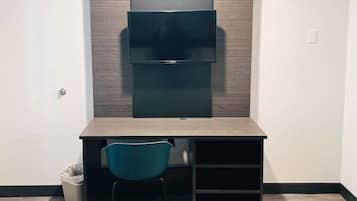 Une pièce compacte et moderne, dotée d’un bureau intégré, d’une chaise et d’un téléviseur fixé au mur.