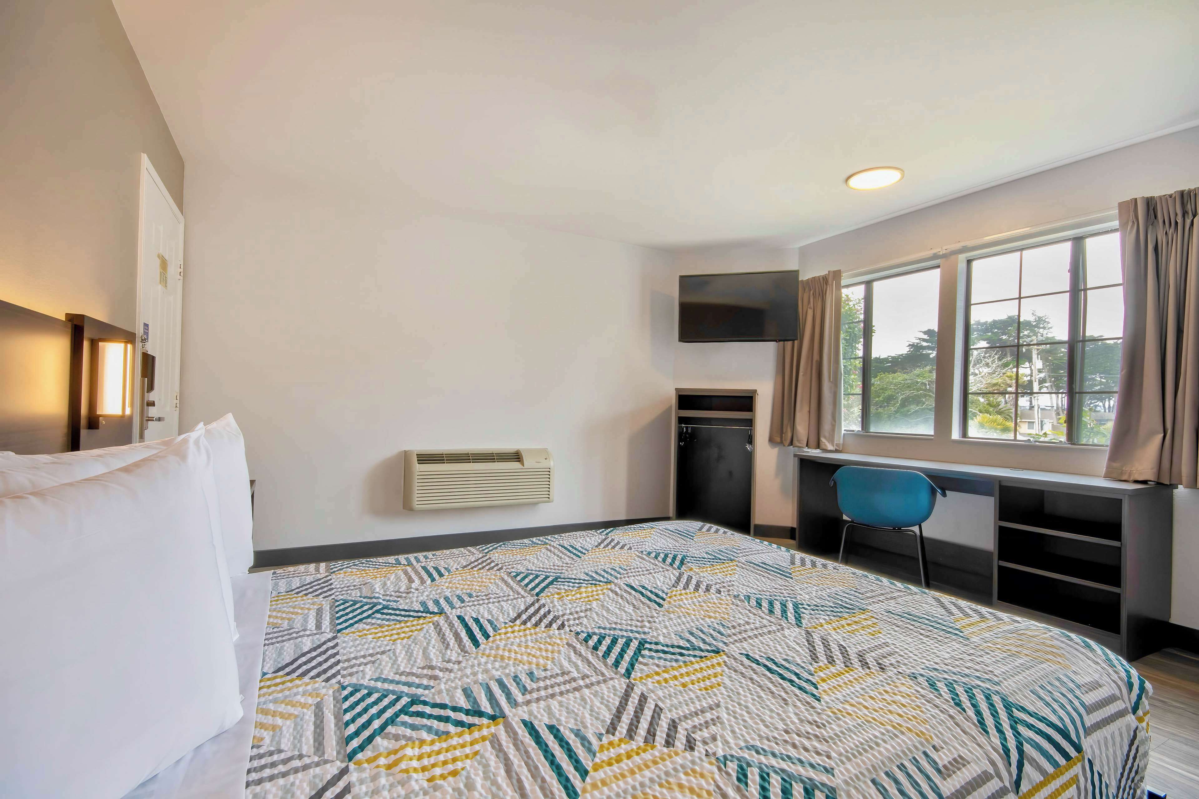 A hotel room with a bed, a desk, a chair, a TV, and a window with curtains.