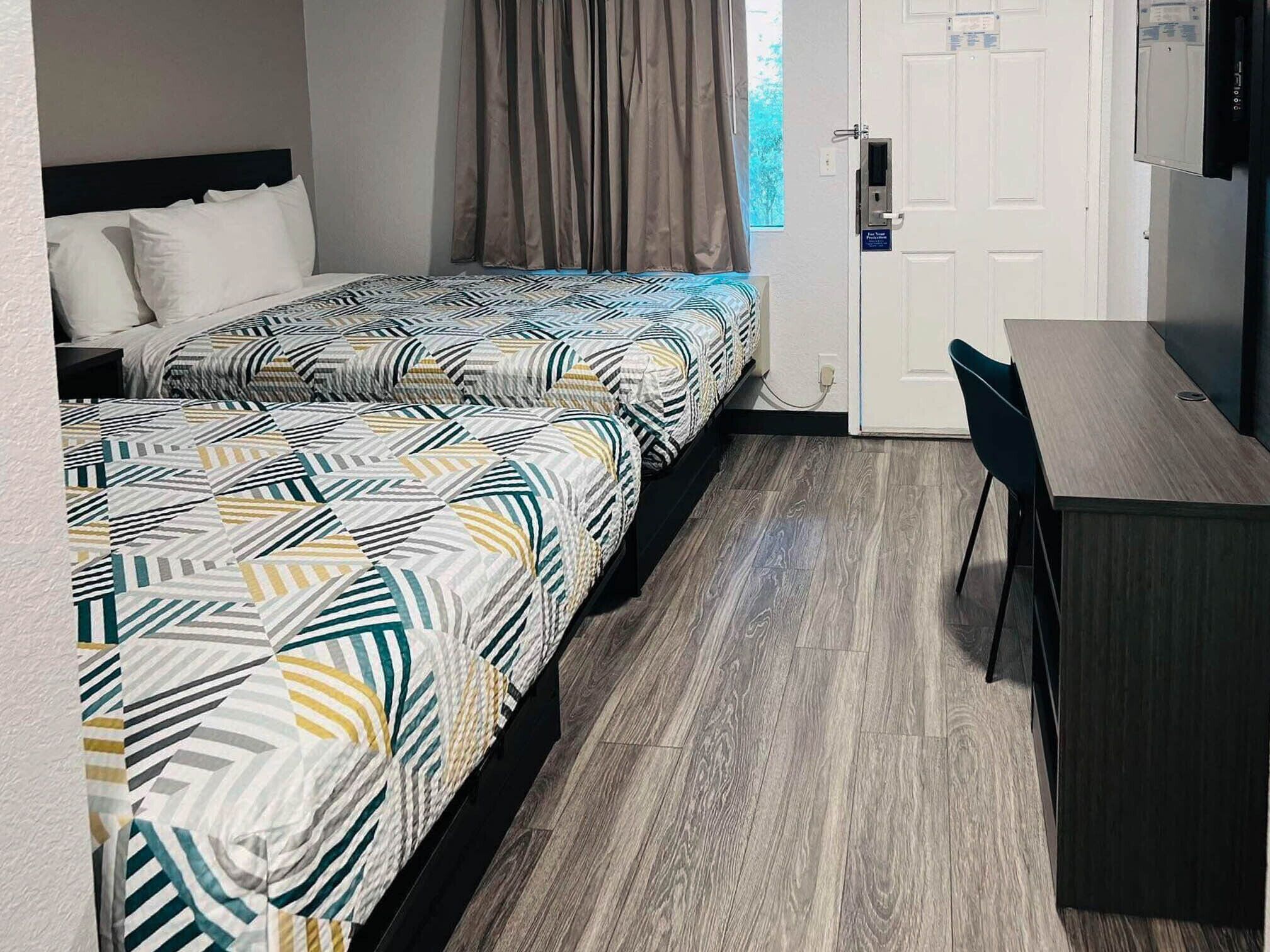 A hotel room with two beds, a desk, and a chair.