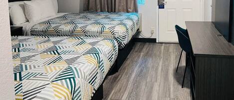 A hotel room with two beds, a desk, and a chair.