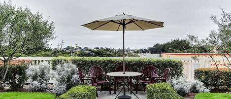 A patio with a round table and chairs, an umbrella, and well-maintained hedges.