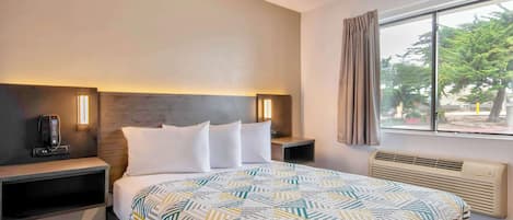 Habitación de hotel con cama, mesitas de noche, teléfono, calefactor y ventana con cortinas.