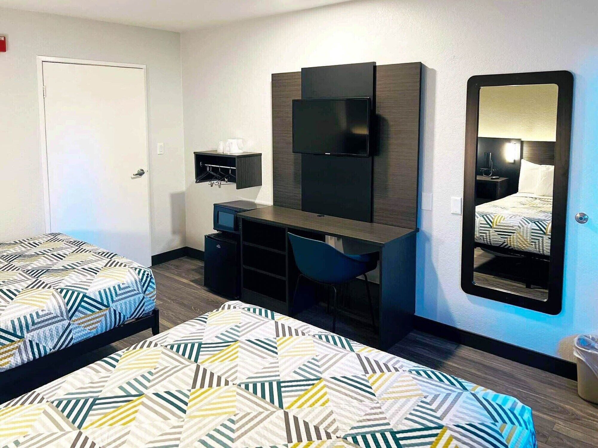 Ein Hotelzimmer mit zwei Betten, einem Schreibtisch, einem Stuhl, einem Fernseher und einem Spiegel.