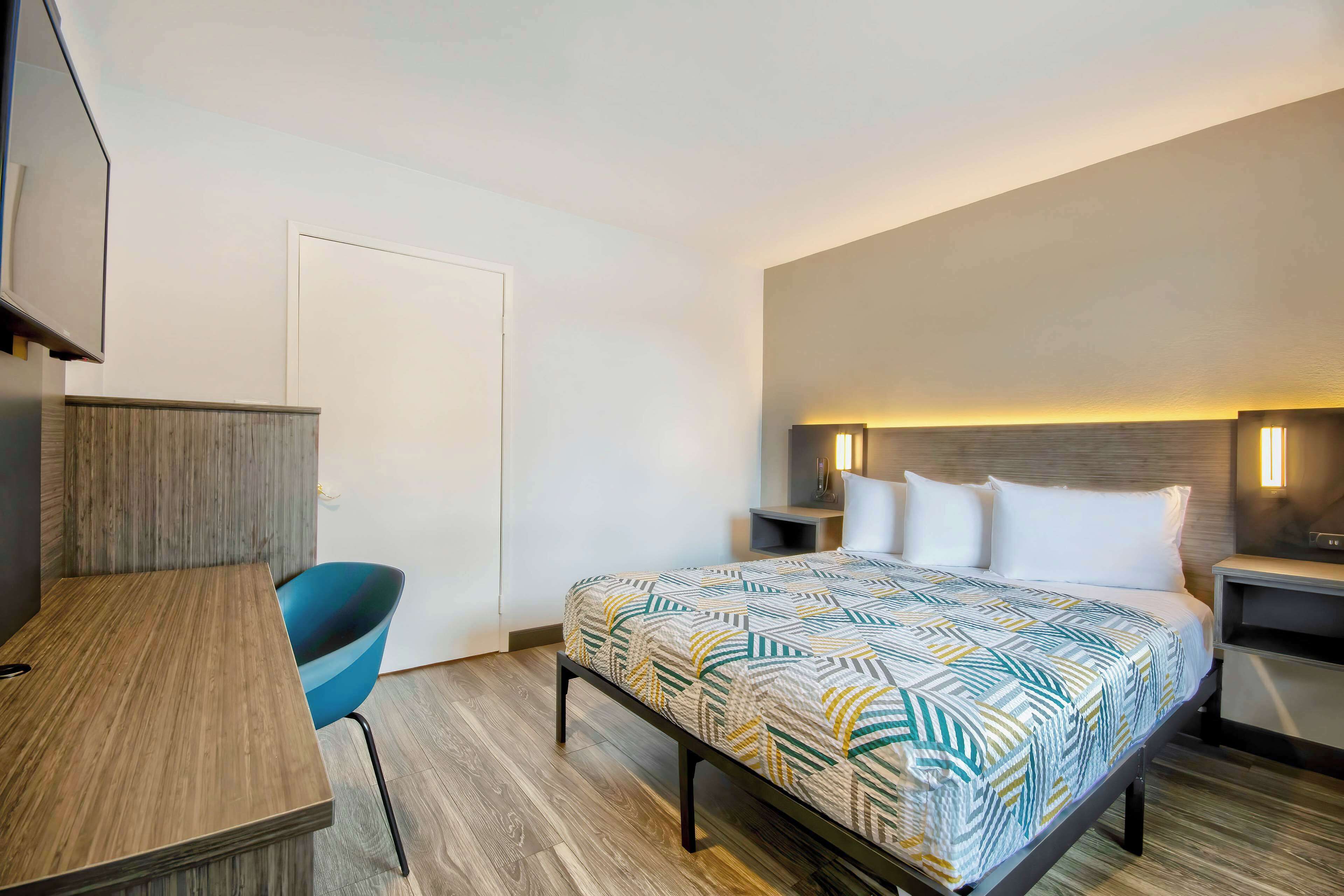 A hotel room with a bed, a desk, a chair, and a TV.