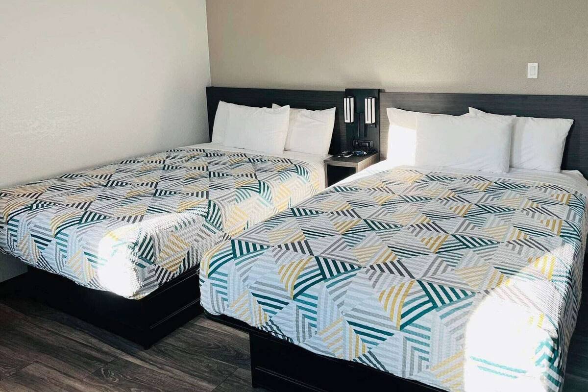 Ein Doppelbett mit geometrischem Bettbezug, ein Nachttisch mit Lampe sowie eine Wandleuchte.