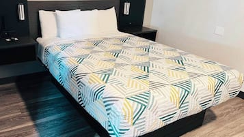 A neatly made bed with a geometric patterned bedspread, a dark headboard, and a bedside table with a lamp.