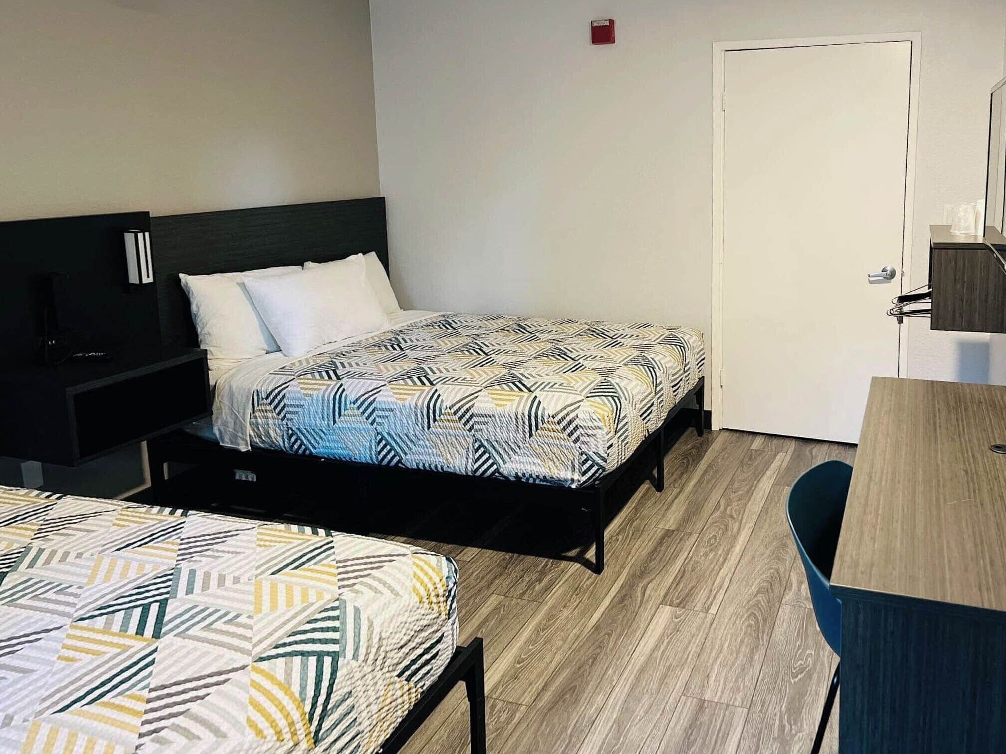 A hotel room with two single beds, a desk, and a chair.