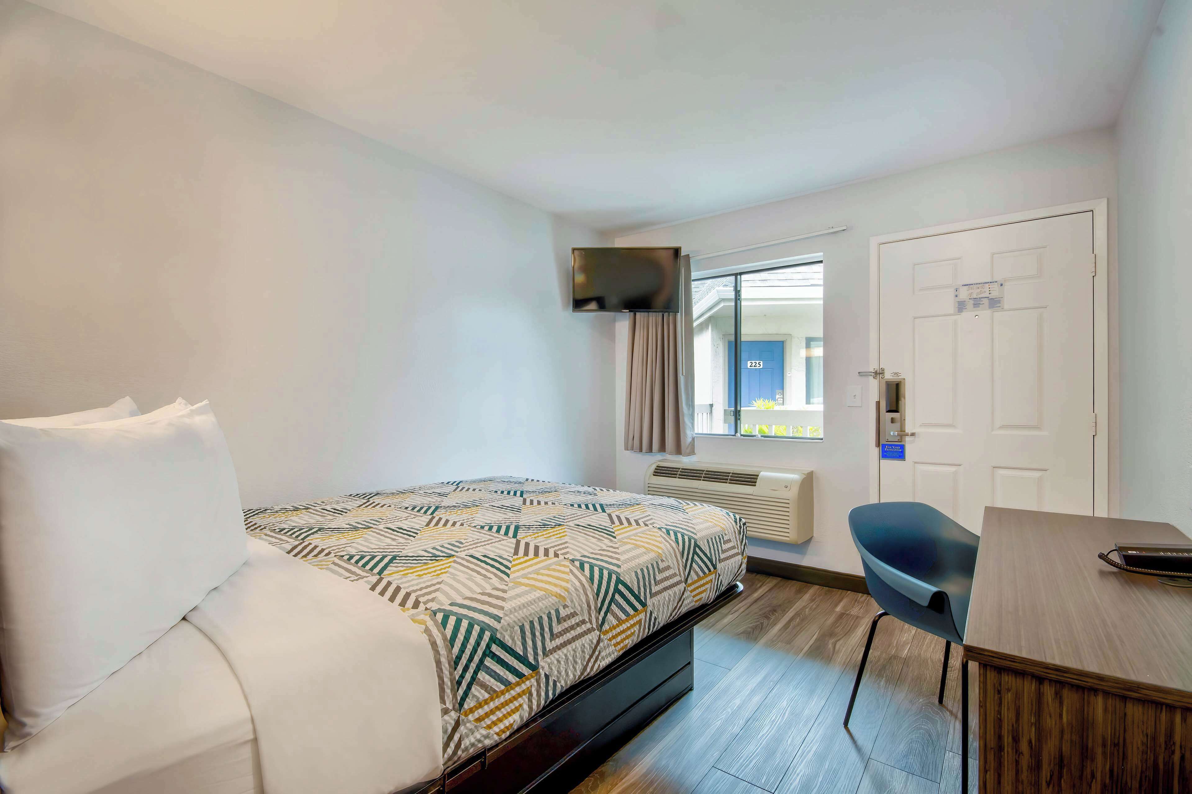 Habitación de hotel con cama, escritorio, silla, ventana y puerta.