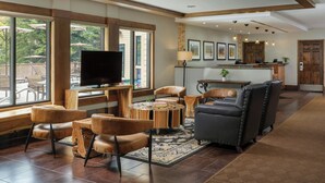 A spacious living area with a large window, leather furniture, a flat-screen TV, and a kitchen in the background. - Marriott's StreamSide Evergreen at Vail (Vail)