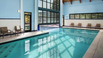 Una piscina interior con agua cristalina y azul, rodeada de sillones de descanso y ventanas amplias.