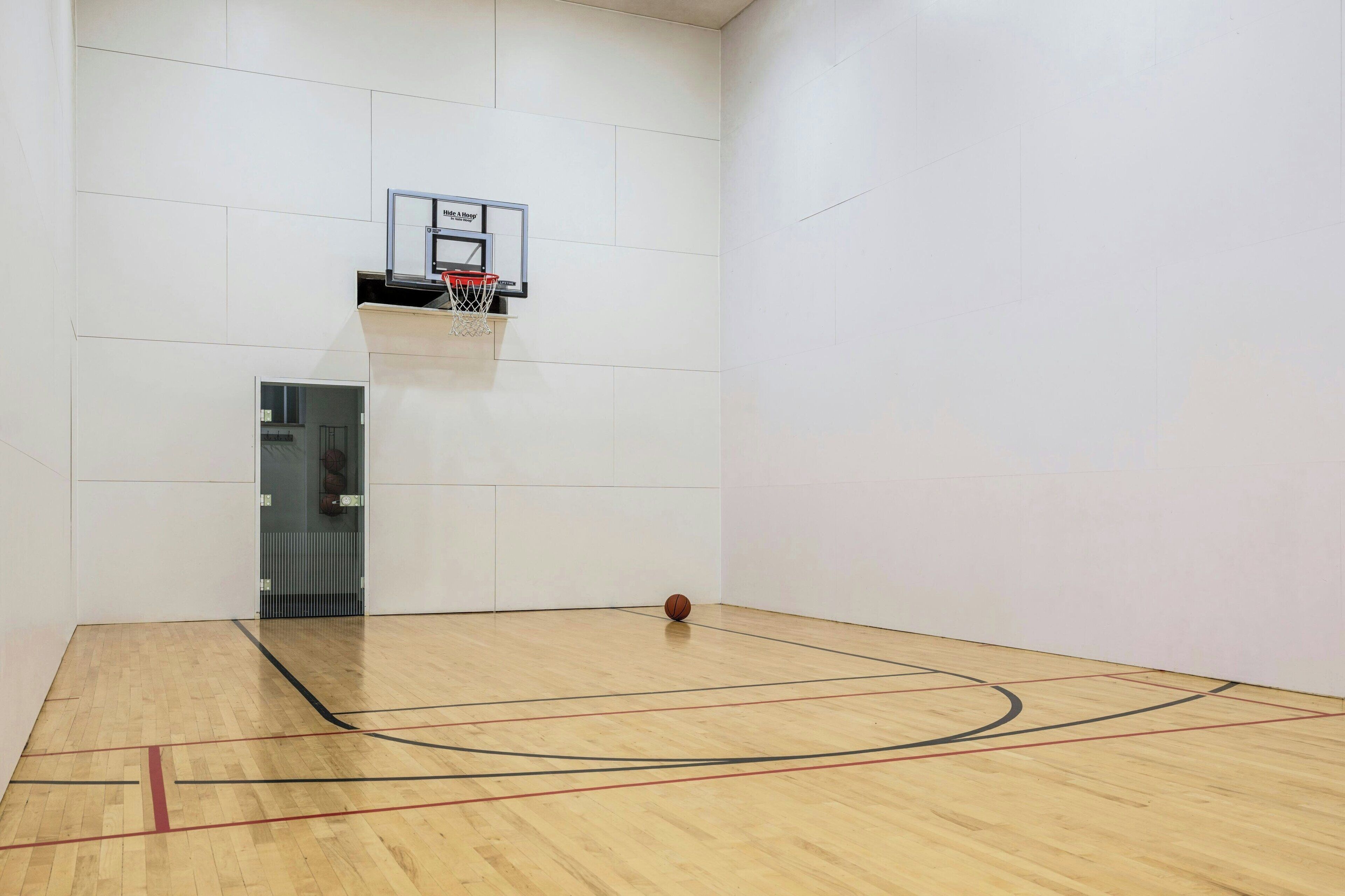 An indoor basketball court with a basketball hoop and a door leading to another room.
