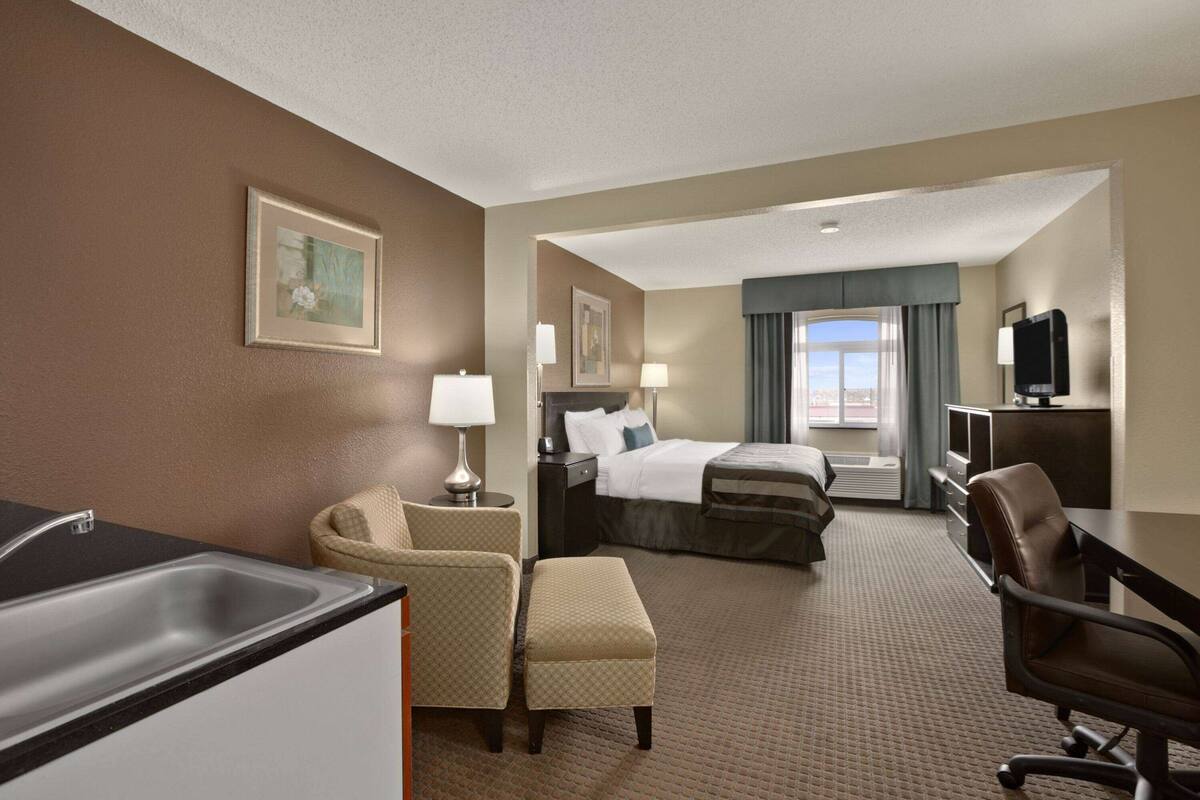 A hotel room with a bed, a desk, a chair, a TV, and a window with curtains.