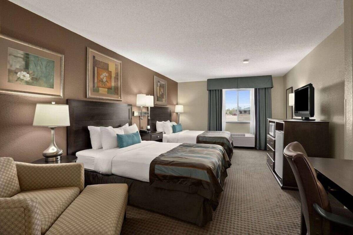 A hotel room with a large bed, two smaller beds, a desk, a TV, and artwork on the walls.
