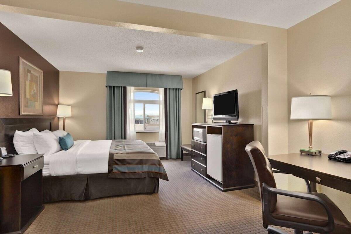 A hotel room with a bed, desk, chair, TV, and a window with curtains.