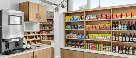 A kitchen area with a coffee machine, shelves stocked with snacks and beverages, and wooden cabinets.
