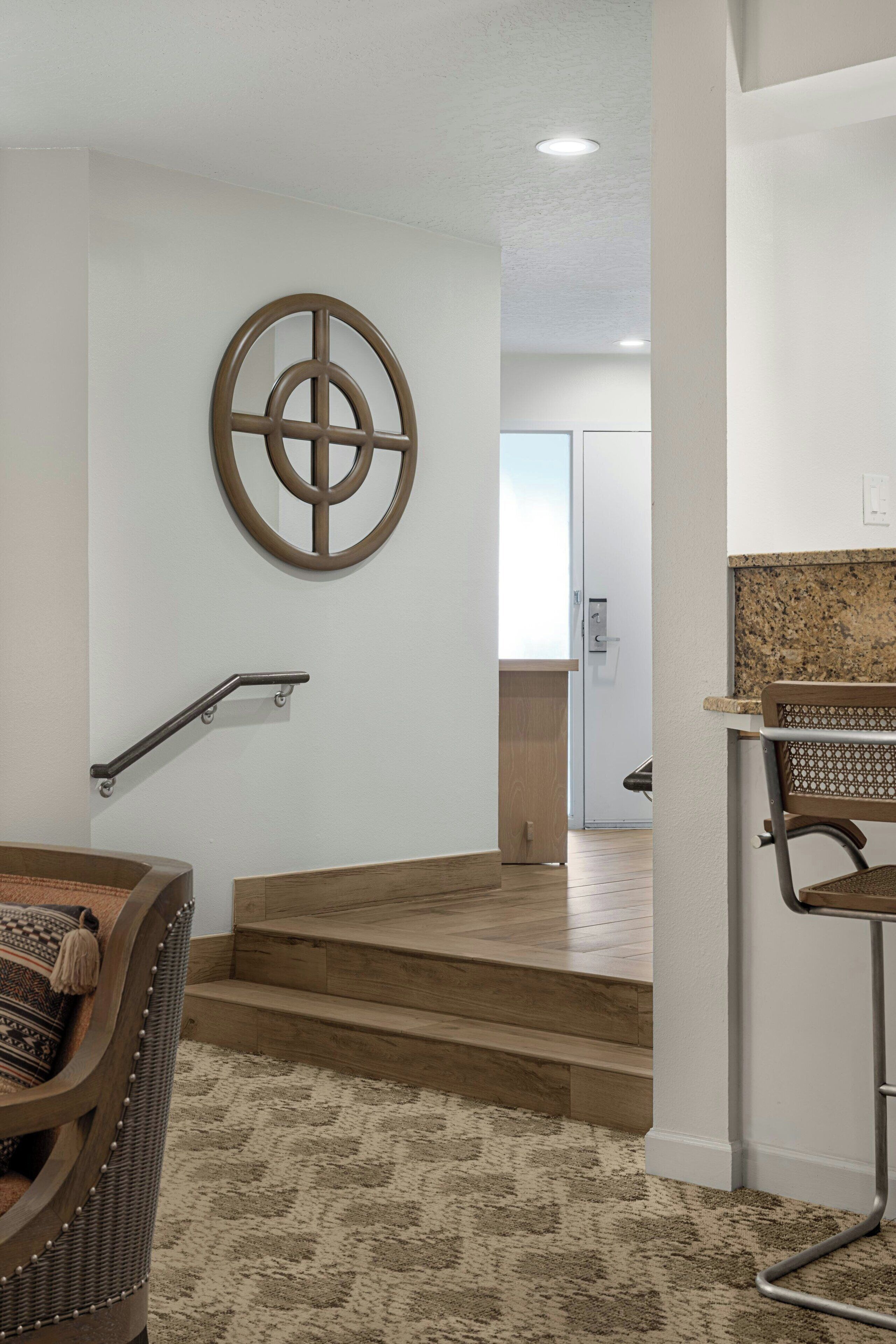 Un interior moderno con una escalera, un diseño circular montado en la pared, un banco de madera y una zona de cocina con encimera y silla.