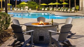 A poolside area with a fire pit surrounded by Adirondack chairs, a pool, and lounge chairs with umbrellas. - Marriott's Sabal Palms (Orlando)