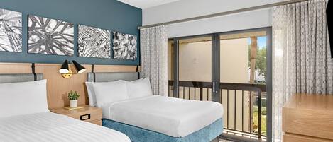 A hotel room with two beds, a ceiling fan, artwork on the wall, a nightstand with a lamp, and a view through a large window.