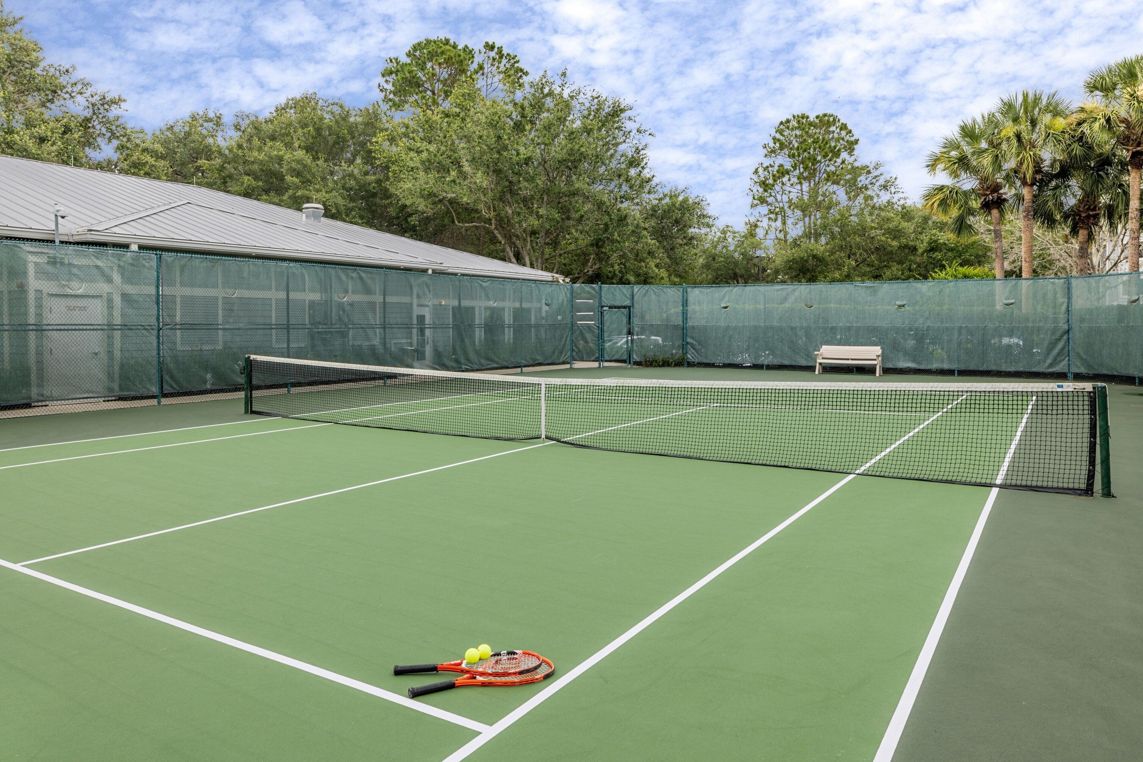 A tennis court with a net, a bench, and tennis rackets and balls.