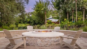 A circular stone fire pit with two Adirondack chairs facing it, surrounded by a paved patio area.