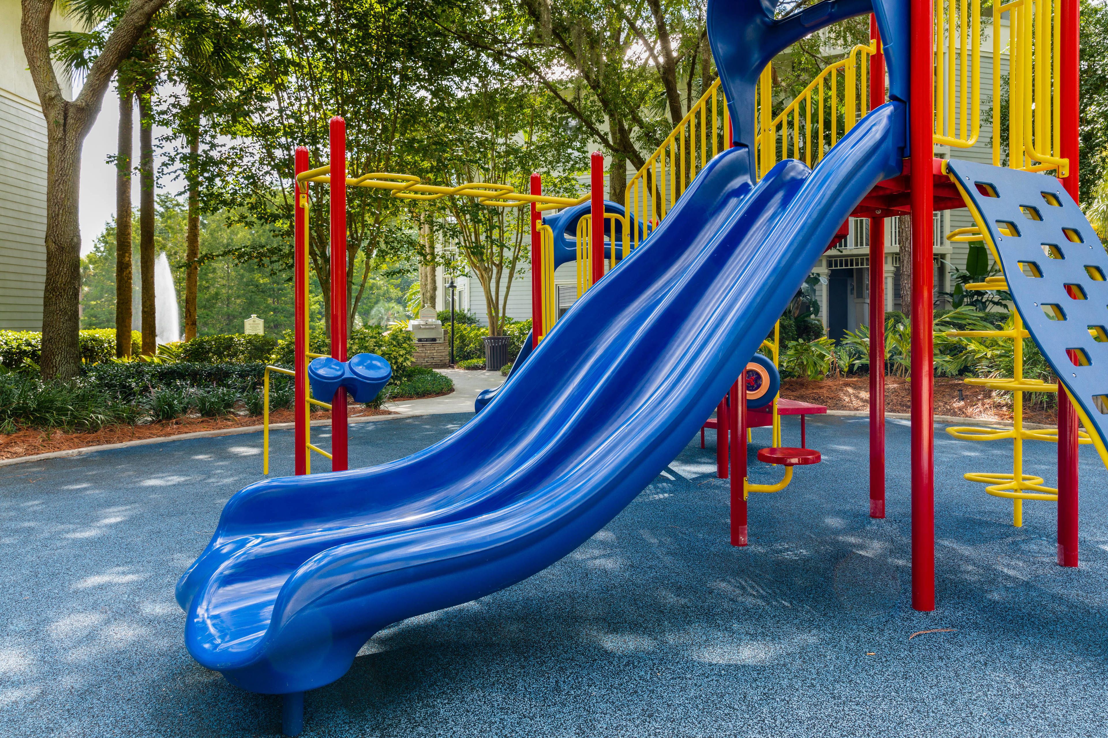 A playground with a blue slide, red and yellow climbing structures, and a blue rubberized floor.