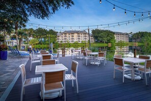Une terrasse extérieure avec des tables et des chaises, offrant une vue sur une étendue d’eau et un immeuble doté de nombreux balcons.