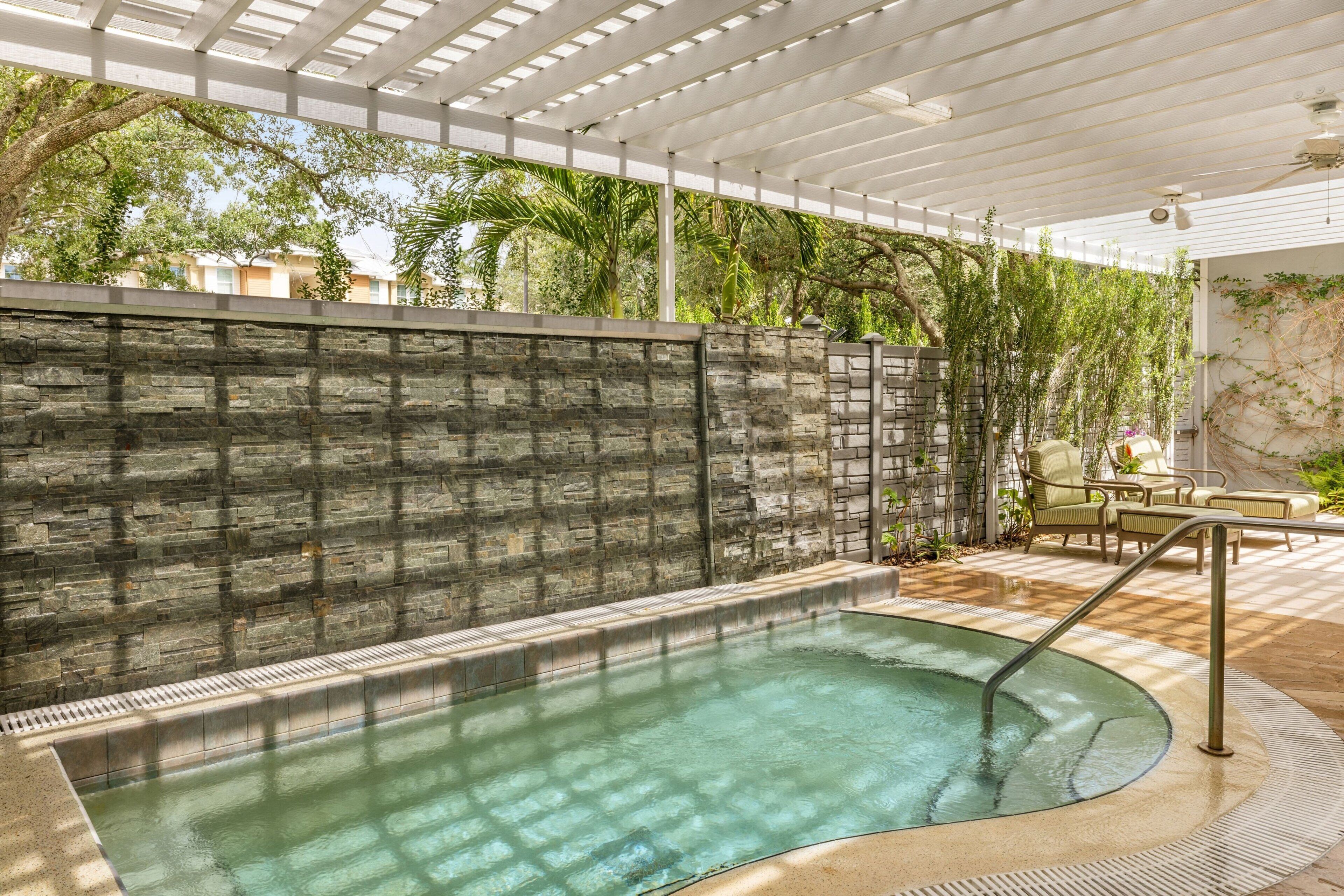 Ein Wellnessbereich mit Steinwand, Whirlpool und Gartenmöbeln.