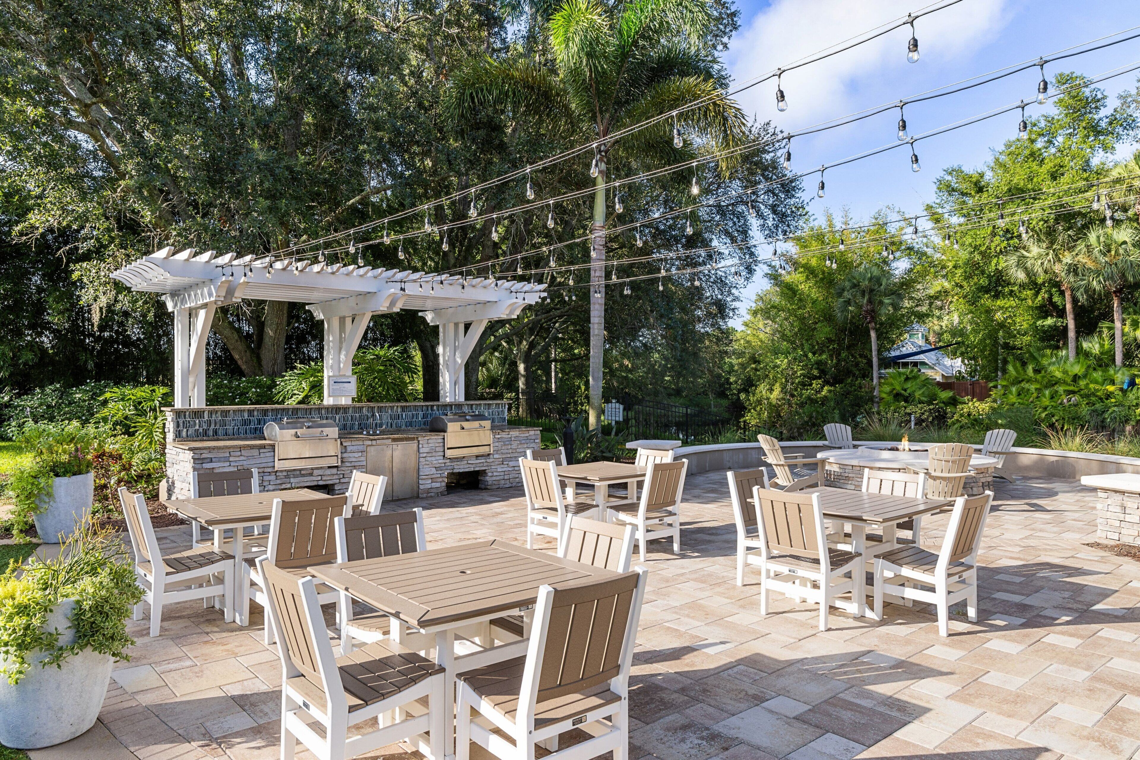 An outdoor patio with multiple tables and chairs, a pergola, and a barbecue area.
