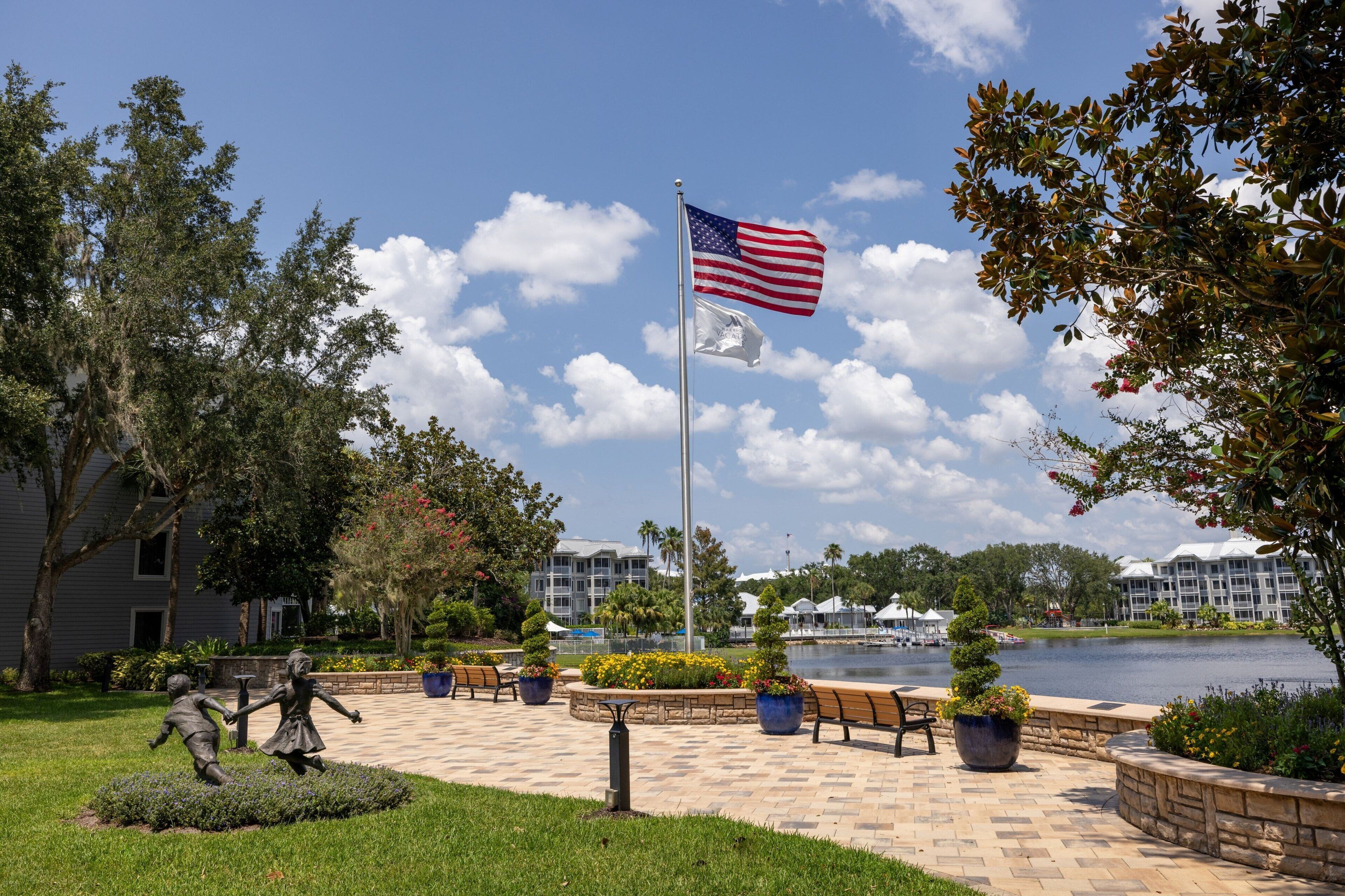 Een vlaggenmast met een Amerikaanse vlag, een standbeeld van een jongen en een meisje, en een waterpartij met gebouwen op de achtergrond.