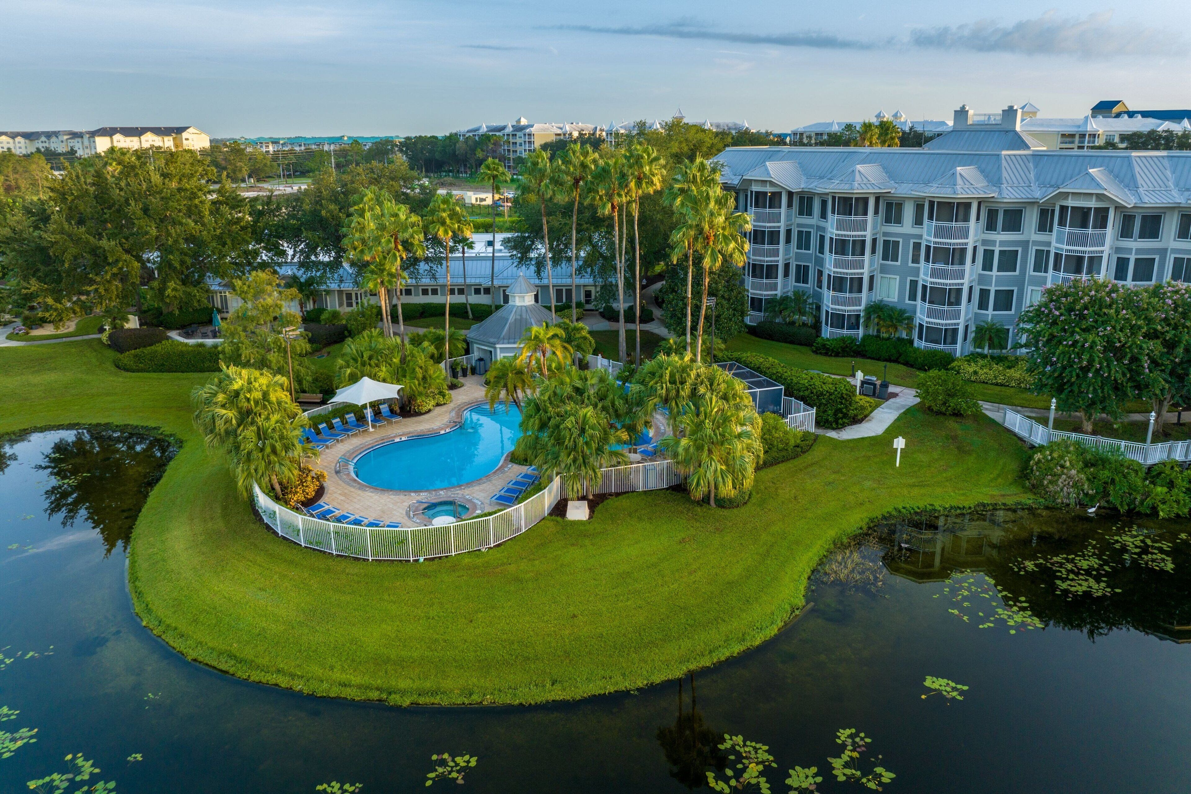 A resort with a swimming pool, palm trees, and a large building with multiple balconies.