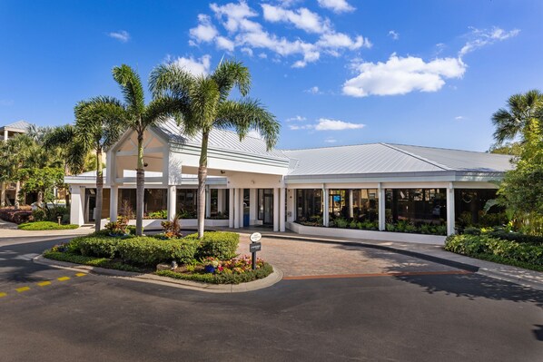 A modern hotel with a covered entrance, palm trees, and a clear blue sky. - Marriott's Imperial Palm Villas (Orlando)