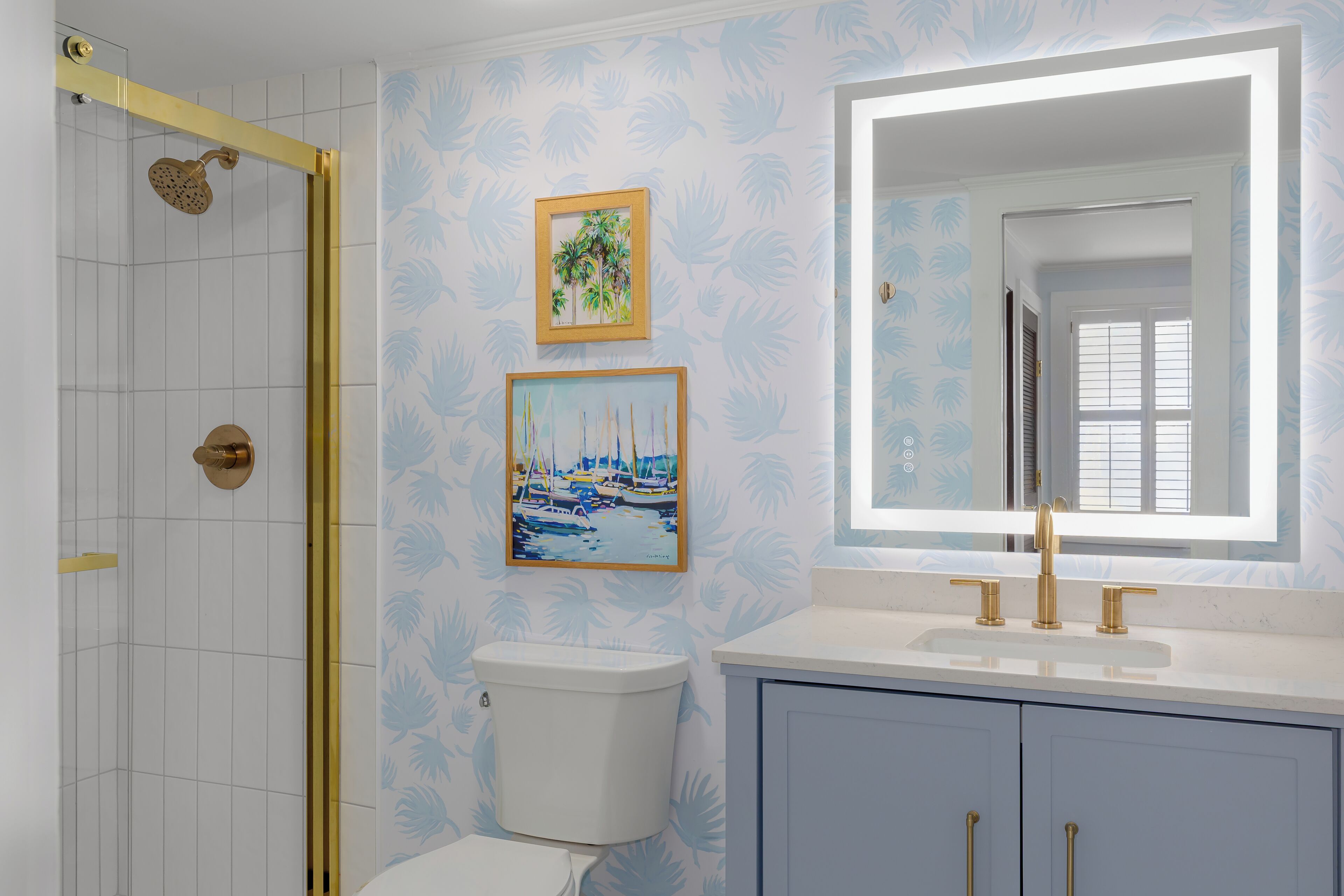 A bathroom with a shower, toilet, sink, and framed artwork on the wall.