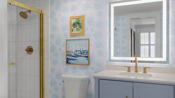 A bathroom with a shower, toilet, sink, and framed artwork on the wall.