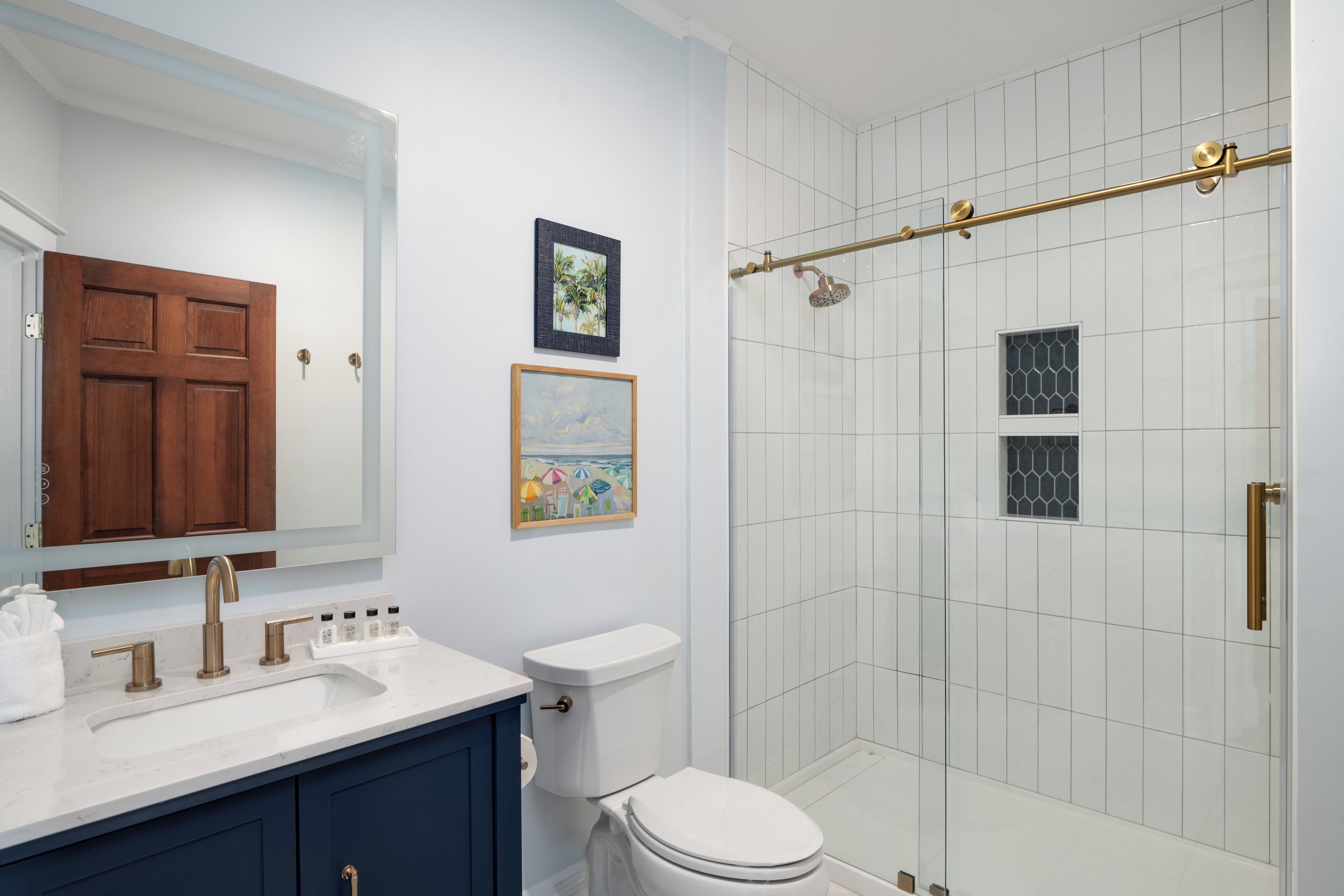 A bathroom with a white toilet, a sink with a marble countertop, a wooden cabinet, and a glass-enclosed shower area.