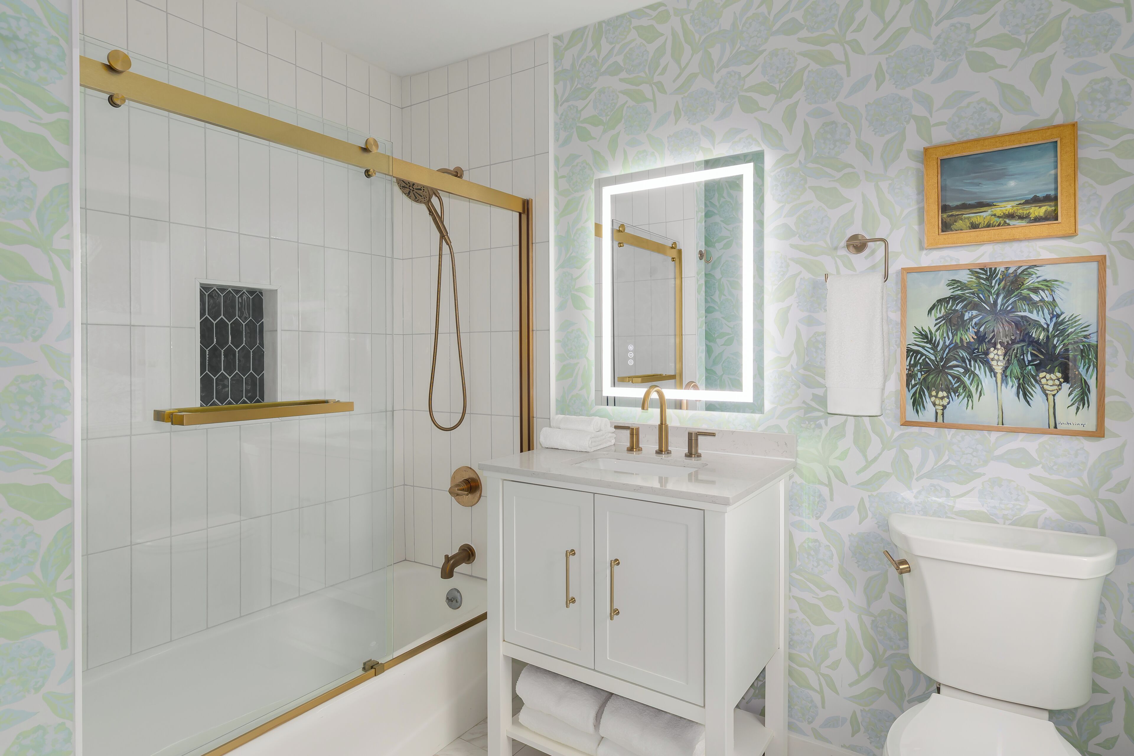 Un baño con ducha, lavamanos con espejo, inodoro y detalles decorativos en la pared.