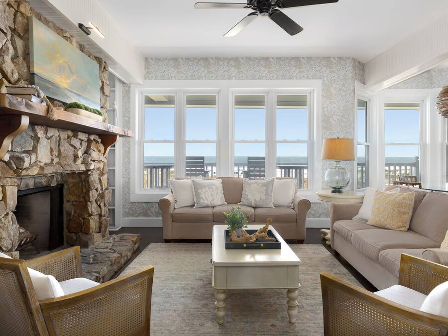 A spacious living room with a stone fireplace, two sofas, a coffee table, and large windows offering a view of the ocean.